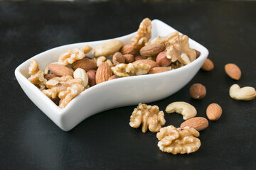 Assorted nuts in white shape bowl on black background. Healthy vegan diet
