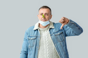 Ill mature man with clothespin on his nose showing thumb-down against grey background