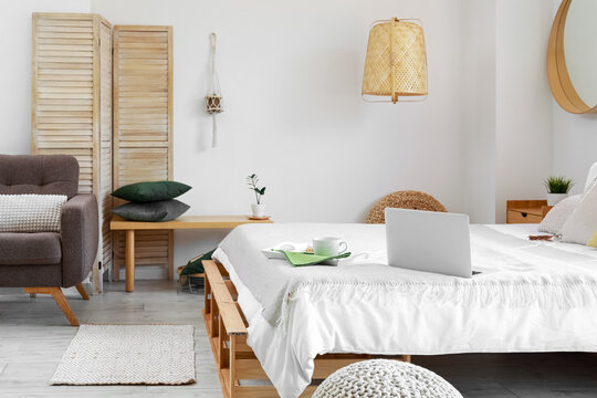 Interior of bedroom with breakfast and laptop on comfortable bed