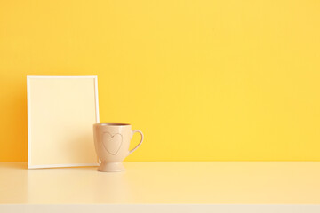 Blank photo frame and cup on table near color wall
