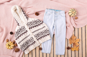 Warm baby clothes and autumn decor on fabric background