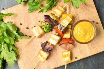 Board with grilled tofu cheese skewers and mustard on dark background