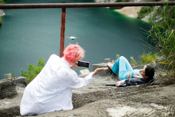 Asian Woman Photographer hold mobile phone camera point to shoot lying woman over cliff