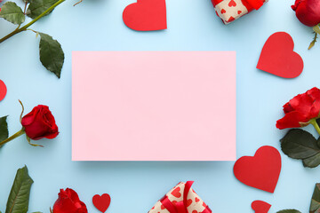 Composition with blank card, rose flowers and paper hearts on blue background. Valentine's Day celebration