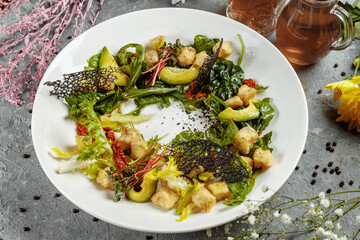 Avocado salad with baby spinach and pomegranate on a black plate on a slate,stone or concrete background.Top view with copy space
