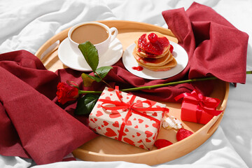 Wooden tray with delicious breakfast and presents for Valentine's Day on soft bed