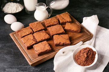 Wooden board with pieces of tasty chocolate brownie on black background