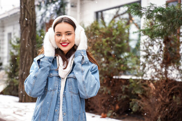 Beautiful young woman wearing mittens and earmuffs on snowy day - obrazy, fototapety, plakaty
