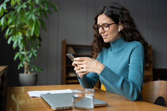 Young Businesswoman Use Smartphone Online Apps For Business Social Media Management And Ads. Female Distance Manager Worker Checking Email Messages On Mobile Phone Sitting At Desk With Closed Laptop