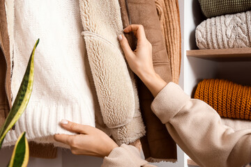 Woman with warm jacket and knitted sweater in wardrobe, closeup