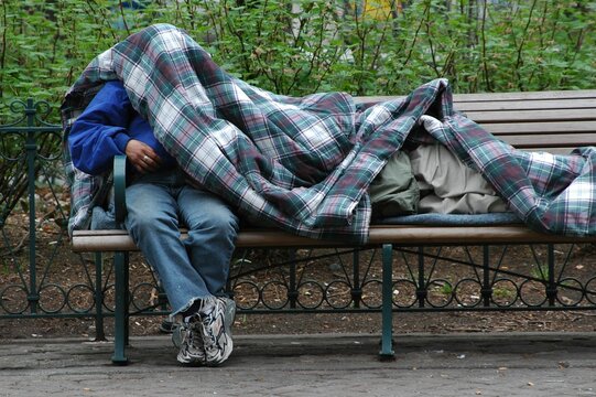 Homeless Men Sleeping On Park Bench In Cold Weather Outside.