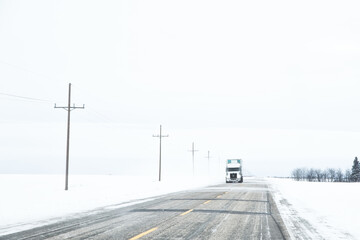 Oncoming eighteen-wheeler on a highway drifting with snow in a countryside winter landscape