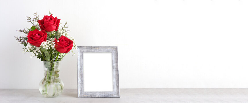 Valentine’s day concept, Red roses flower bouquet in glass vase and blank grey vintage wooden frame on table background with copy space , Banner for mock up, template
