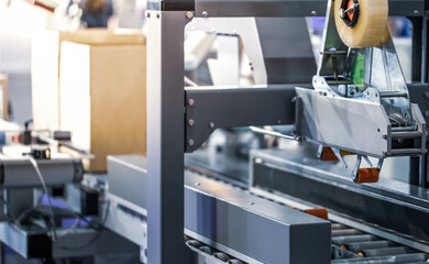 Automated carton, cardboard tape sealing machine. Industrial logistics warehouse.	