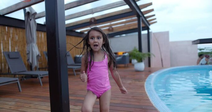 Adorable excited little girl running on wooden pool deck
