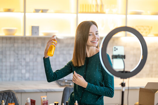 Smiling young woman presenting hairspray during online beauty tutorial