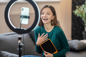 Cheerful young woman in green shirt in front of camera making online workshop