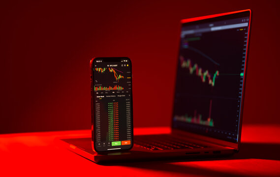 The evolution of the crypto currency coin industry. Detail view of a smartphone in front of a laptop while following the stock market movement. Concept for this new financial trend. Red background.