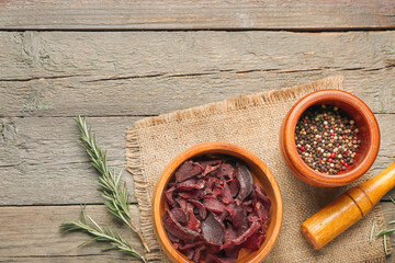 Bowl with spicy beef jerky on wooden background
