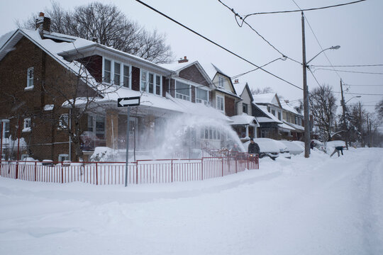 Toronto, Ontario / Canada - January 17, 2022 - Toronto St Clair West sideroad on day of snowstorm and man snowblowing