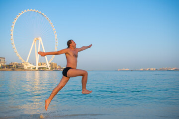 a man in swimming trunks jumping on the beach in the uae