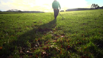 An anonymous metal detectorist searching for a 'find' in a field with the sun behind him.