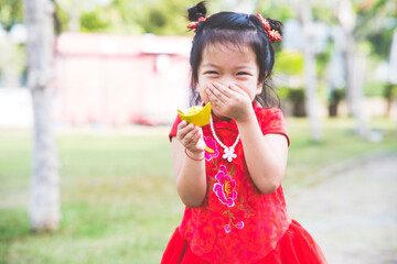 Portrait of Asian kid girl was laughing. Child wear red cheongsam. Child holding gold money in traditional Chinese style. Empty space to enter text. Happy Chinese New Year Concept.
