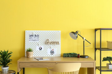 Stylish workplace with peg board on yellow wall background