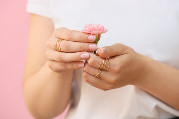 Woman with beautiful manicure and stylish jewelry holding beautiful carnation flower on color...