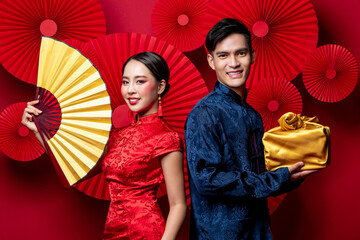 Smiling Asian couple in traditional costumes with fan and gold package as a gift for Chinese new...