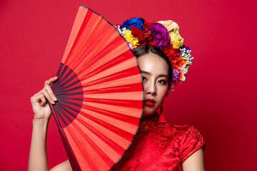 Beautiful Asian woman wearing traditional dress with flower chaplet holding red fan in isolated studio background for Chinese new year concept - obrazy, fototapety, plakaty