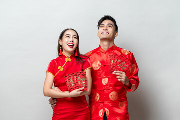 Asian couple in traditional oriental costumes holding red envelopes or Ang Pow in gray background...