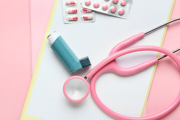 Clipboards, stethoscope, pills and asthma inhaler on color background, closeup