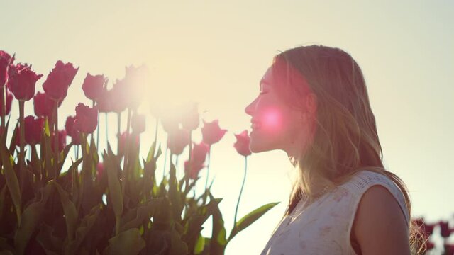 Closeup woman face profile smelling flowers in sun reflecction bright sunny day.