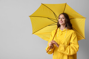 Beautiful smiling woman in yellow raincoat with opened umbrella on grey background