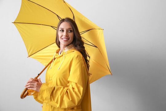 Beautiful woman in yellow raincoat with opened umbrella on grey background