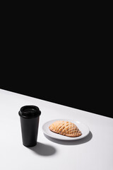 Freshly armadillo baked Mexican artisan bread on a white plate on a white table and a black wall in the background with a black cup of coffe