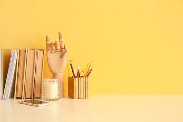 Books, wooden mannequin hand, stationery holder and mobile phone on table near color wall - obrazy, fototapety, plakaty