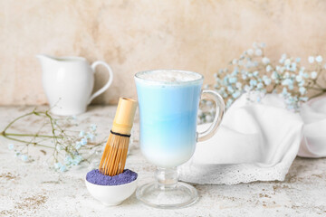 Glass of blue matcha latte, powder and chasen on light background