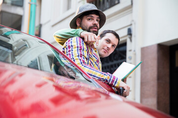 A latin gay tourist couple on a red car looking for directions  in the city.