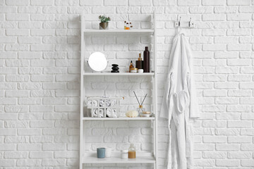 Shelving unit with bath supplies and bathrobe hanging on white brick wall