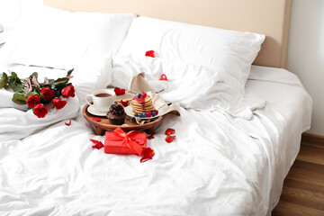 Wooden tray with delicious breakfast, roses and present for Valentine's Day on soft bed in bedroom