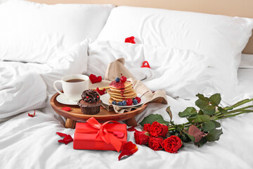 Wooden tray with delicious breakfast, roses and present for Valentine's Day on soft bed