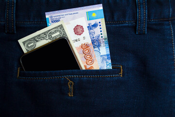 Banknotes of different countries with a phone in the back pocket of Jeans. Traveling with different currencies. tenge, dollar, ruble.