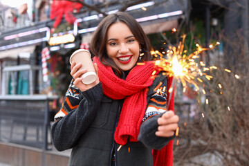 Fototapeta premium Young smiling woman with paper cup and sparkler on winter day