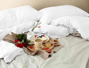 Fototapeta na wymiar Wooden board with tasty breakfast and bouquet of roses for Valentine's Day on bed
