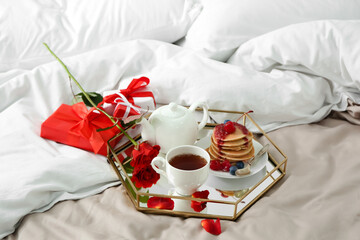 Fototapeta na wymiar Tray with tasty breakfast, rose flower and gift boxes for Valentine's Day on bed