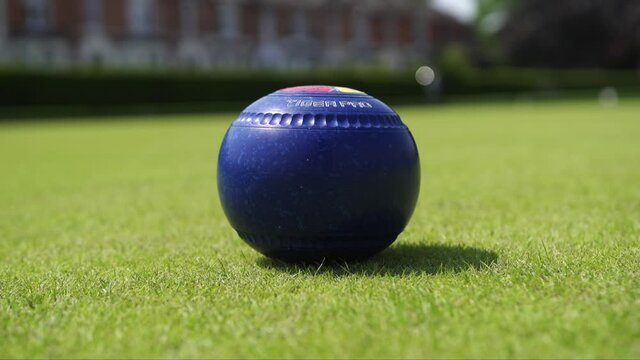A single bowl being hit on the green in England on a summers day.