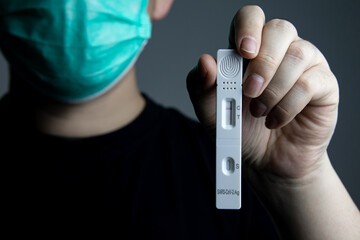 Close-up of man wearing mask showing negative antigen kit to test himself for COVID-19 omicron...