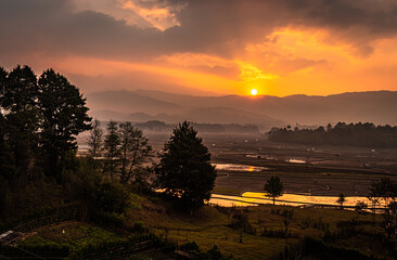 Obraz premium sunrise over mountains with country side farming fields and orange dramatic sky at dawn at village
